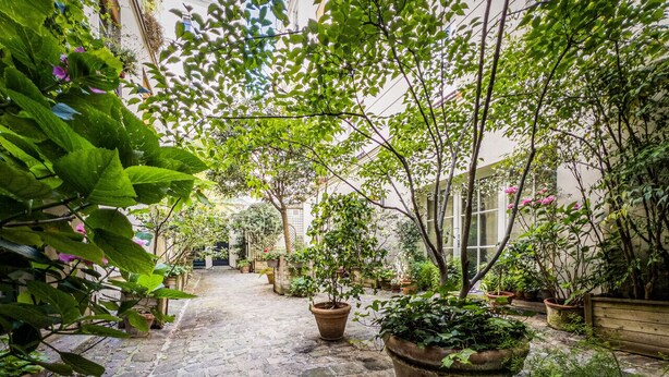 Une petite cour dallée de pierres, agrémentée de plantes en pot et d’un banc en bois.