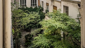 Une cour étroite, bordée de bâtiments de chaque côté, avec des balcons ornés de jardinières et un mur de pierre en premier plan.