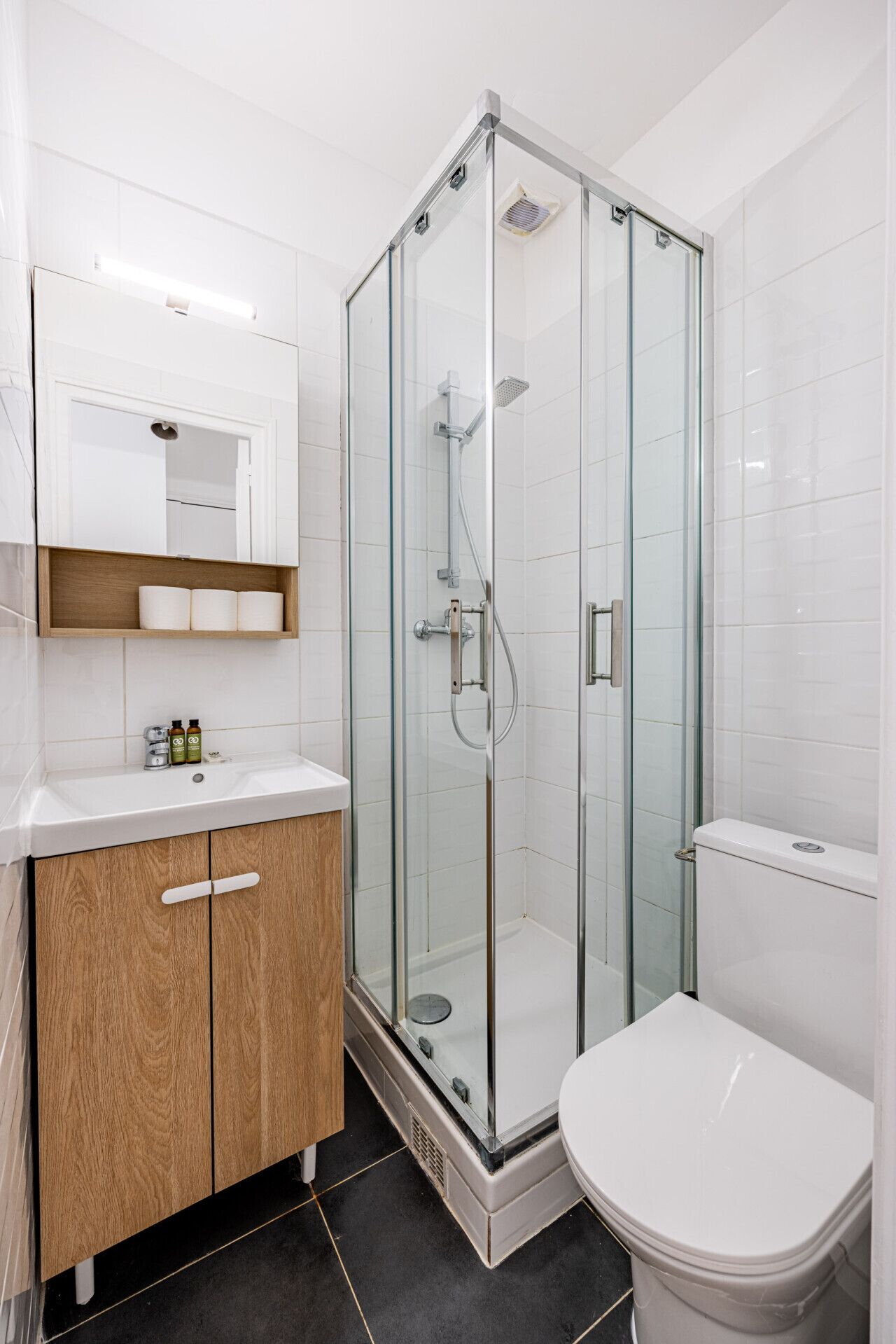 Et moderne badeværelse med en glasbrusekabine, et træbord med et spejl og et hvidt toilet.