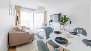 Un salon moderne avec un canapé, une table à manger dressée avec des assiettes et des verres, et un téléviseur fixé au mur.
