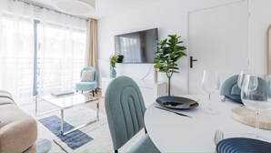 Un salon moderne comprenant un coin repas, un téléviseur à écran plat fixé au mur, une plante en pot et une table à manger dressée avec des assiettes et des verres à vin.