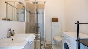 A modern bathroom with a glass shower enclosure, a white sink with a towel, a toilet, and a washing machine.