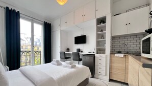 A modern hotel room with a bed, a desk, a TV, and a kitchenette.