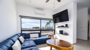 A modern living room with a blue leather sectional sofa, a wooden coffee table, and a large window offering a city view. - Casa Diamante 65 - Spacious residence with private pool in Biznaga, San Carlos, Mexico (guaymas)