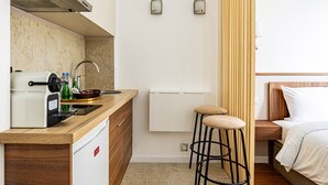 A compact hotel room with a kitchenette, a bed, and a small stool.
