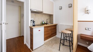 A compact kitchen with a built-in refrigerator, a sink, and a small countertop. There is a stool and a cabinet with a wooden finish.