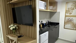 A compact kitchen with a built-in microwave, a small refrigerator, and a dining area with a chair and a vase of flowers. - Cabo Branco | Studio + Rooftop Pool (João Pessoa)