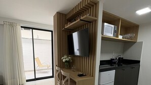 A modern kitchen with a built-in microwave, a dining area with a chair, and a TV mounted on a wooden panel. - Cabo Branco | Studio + Rooftop Pool (João Pessoa)