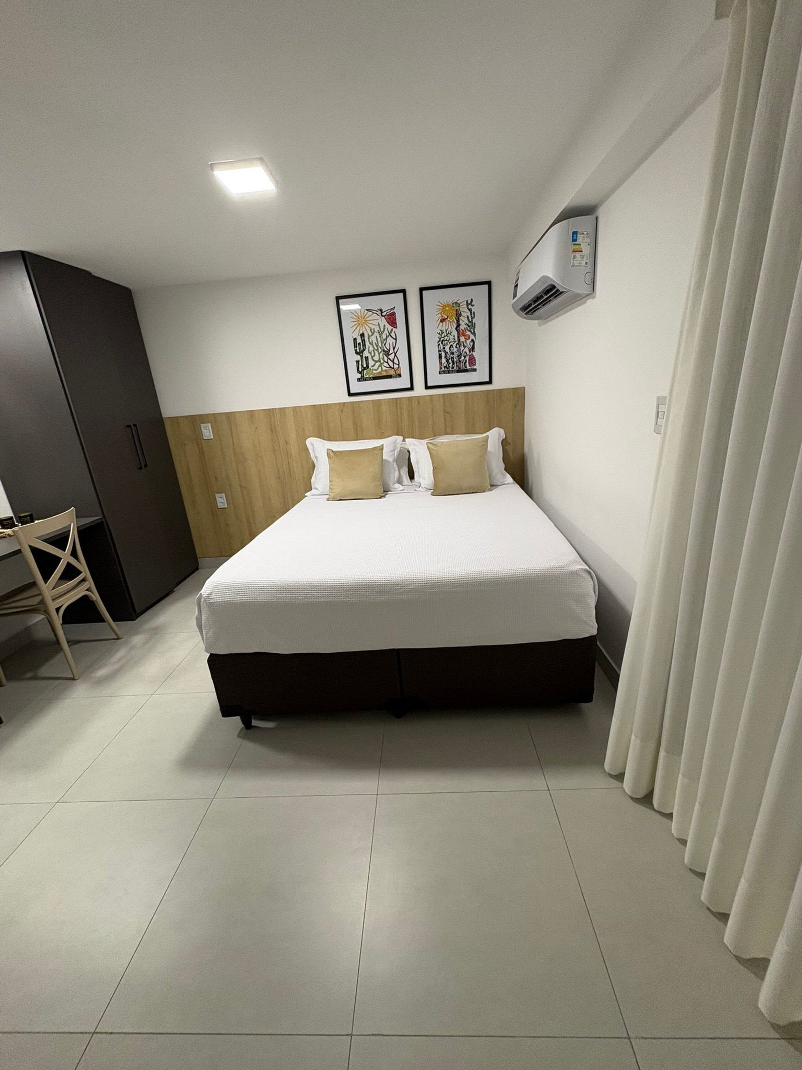 A hotel room with a bed, a wardrobe, a desk, and two wall-mounted air conditioning units.