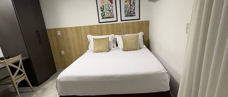 A hotel room with a bed, a wardrobe, a desk, and two wall-mounted air conditioning units.