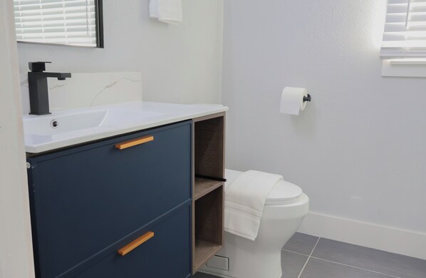 Une salle de bain moderne avec un lavabo blanc, un meuble bleu foncé et des toilettes blanches.