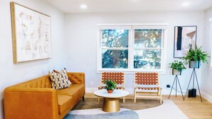 A modern living room with a sofa, chairs, a coffee table, and a large window with a view of trees.