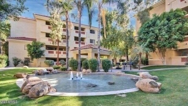 A courtyard with a central water feature, surrounded by palm trees and large rocks.