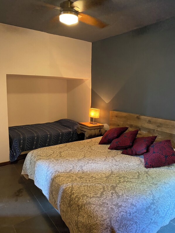 A bedroom with a bed, two bedside tables, a nightstand, a ceiling fan, and a lamp.