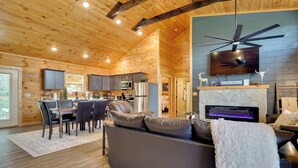 A modern log cabin interior with a dining area, kitchen, living room, and fireplace. - 1 Mi to Douglas Lake: Blissful Escape w/ Hot Tub! (Sevierville)