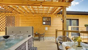 A wooden cabin with a hot tub, outdoor seating, and a table with wine glasses and a bottle. - 1 Mi to Douglas Lake: Blissful Escape w/ Hot Tub! (Sevierville)