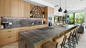 A modern kitchen with a large island, wooden cabinets, and a large window offering a view of greenery. - The Lunith Retreat, Luxury Stay w/ Pool & Spa (Austin)