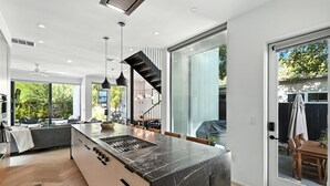 A modern kitchen with a large island, pendant lights, and a view to the outside. - The Lunith Retreat, Luxury Stay w/ Pool & Spa (Austin)