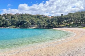 A beach with clear turquoise water, a pebbly shore, and a backdrop of trees and buildings. - Close to the beach, picturesque accommodations with an unparalleled ocean view! (Sibenik)