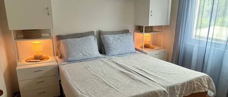 A bedroom with a large bed, two bedside tables with lamps, a ceiling fan, and a window with curtains.
