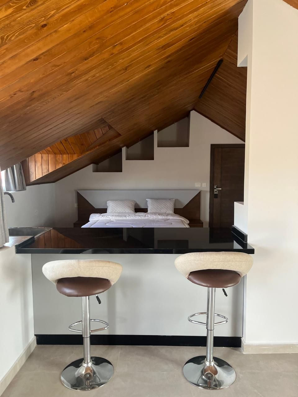 Een knus keuken met een houten plafond, een centraal eiland met krukken, en een bed op de achtergrond.