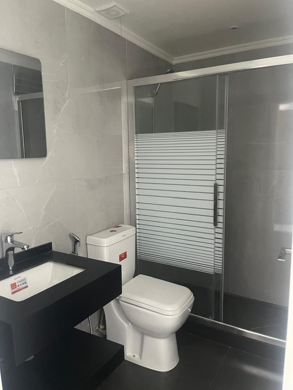 Un baño moderno con un lavabo negro, inodoro blanco y cabina de ducha con paredes de vidrio.