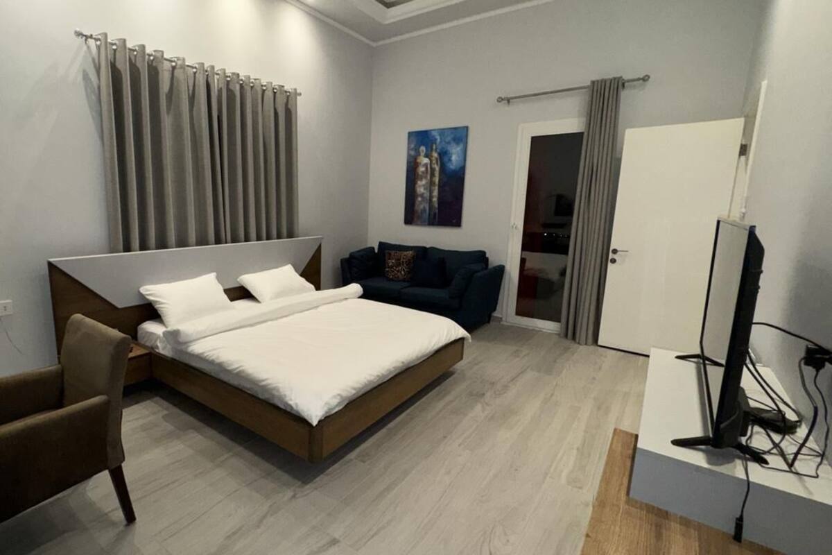 A modern bedroom with a large bed, a sofa, a TV, and a door leading to a bathroom.