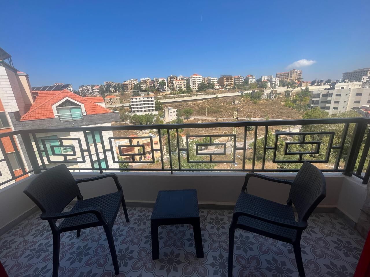Un balcón con dos sillas y una mesa pequeña, con vista a un paisaje urbano de varios edificios.