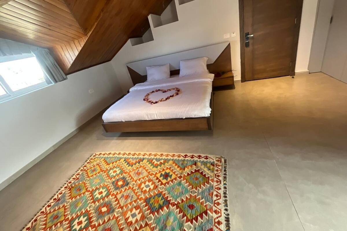 A bedroom with a bed, a patterned rug, and a wooden staircase.