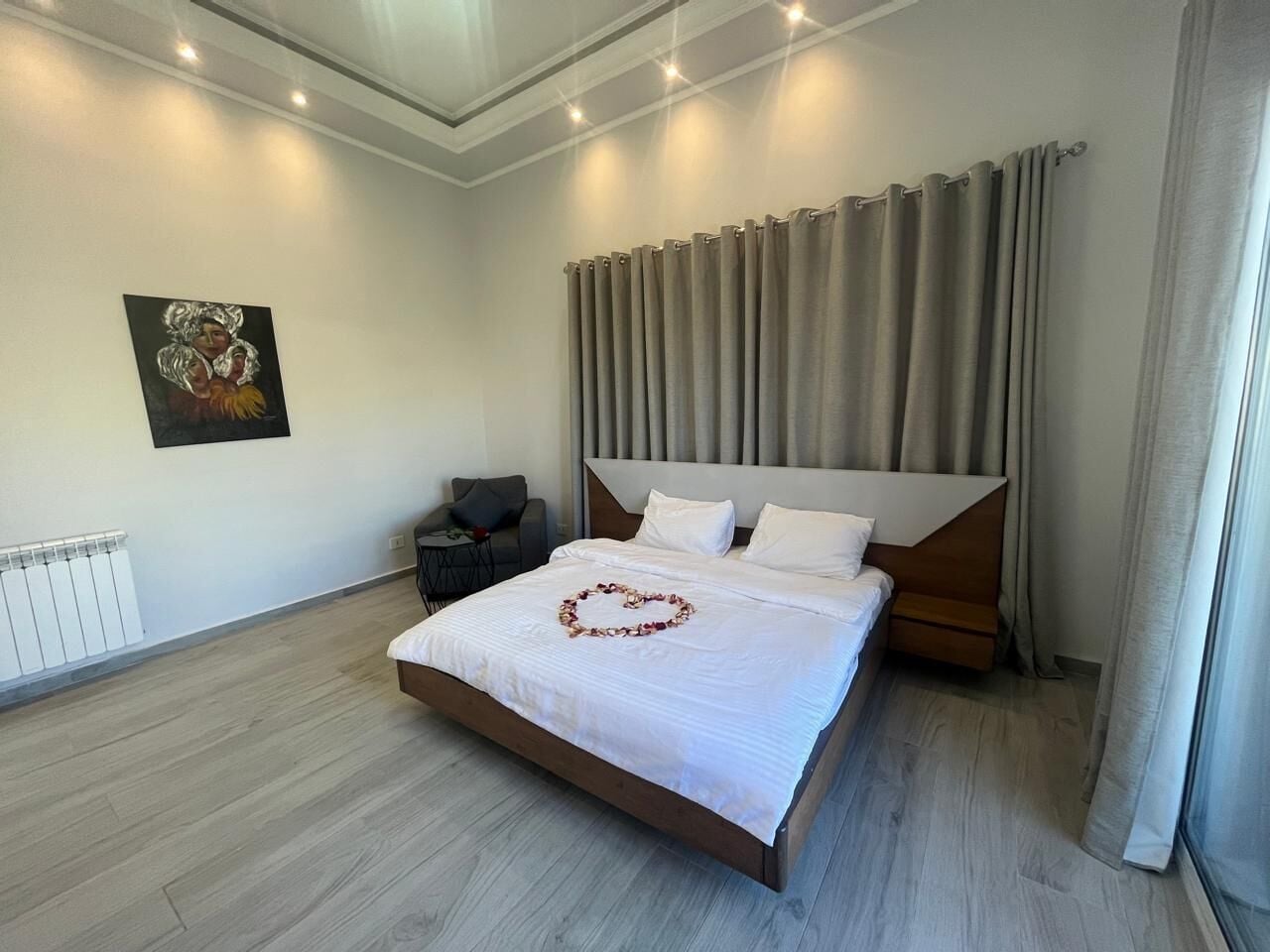 Un dormitorio moderno con una cama grande, cabecera, mesita de noche, radiador y un cuadro en la pared.