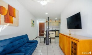 Una sala de estar con un sofá azul, un comedor con mesa y sillas, una cocina con armarios y un televisor montado en la pared.