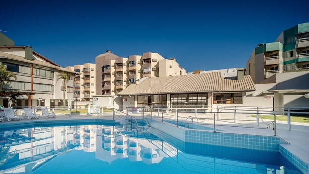 Une piscine avec une terrasse carrelée, un espace salon couvert et un bâtiment doté de plusieurs balcons en arrière-plan.