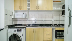 Une cuisine compacte équipée d’un lave-linge, d’un four à micro-ondes et d’un four traditionnel.