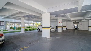 Un parking avec des piliers blancs, une voiture blanche et une entrée de bâtiment portant l’inscription « ALFA ».
