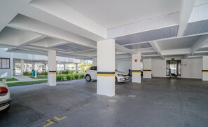 Eine Tiefgarage mit weißen Säulen, einem weißen Auto und einem Gebäudeeingang mit der Aufschrift 'ALFA'.