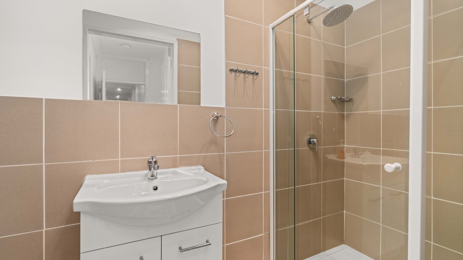 A bathroom with a white sink, a glass shower enclosure, and beige tiles.