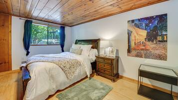 A bedroom with a wooden ceiling, a bed with white linens, a nightstand with a lamp, and a painting on the wall.