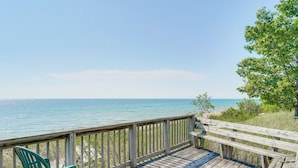 A wooden deck with a view of the ocean, a green chair, and a wooden railing. - Walk to Semi-Private Beach: Lake Michigan Getaway (Montague)