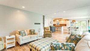 A spacious living room with a sofa, ottoman, and armchair, a small side table, and a view into the kitchen area. - Walk to Semi-Private Beach: Lake Michigan Getaway (Montague)