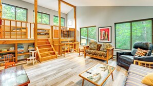 A spacious living area with a wooden staircase, a sofa, a recliner, and a coffee table. - Walk to Semi-Private Beach: Lake Michigan Getaway (Montague)