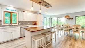 A modern kitchen with a wooden island, bar stools, and a dining area with a wooden table and chairs. - Walk to Semi-Private Beach: Lake Michigan Getaway (Montague)