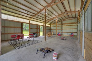 Une grande grange dotée de hauts plafonds et de poutres en bois, comprenant un coin repas avec des chaises et une table, ainsi qu’un espace extérieur couvert avec des chaises et une table.