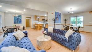 Een ruime woonkamer met een grote blauwe bank, een ronde salontafel en een eethoek met een houten tafel en stoelen.