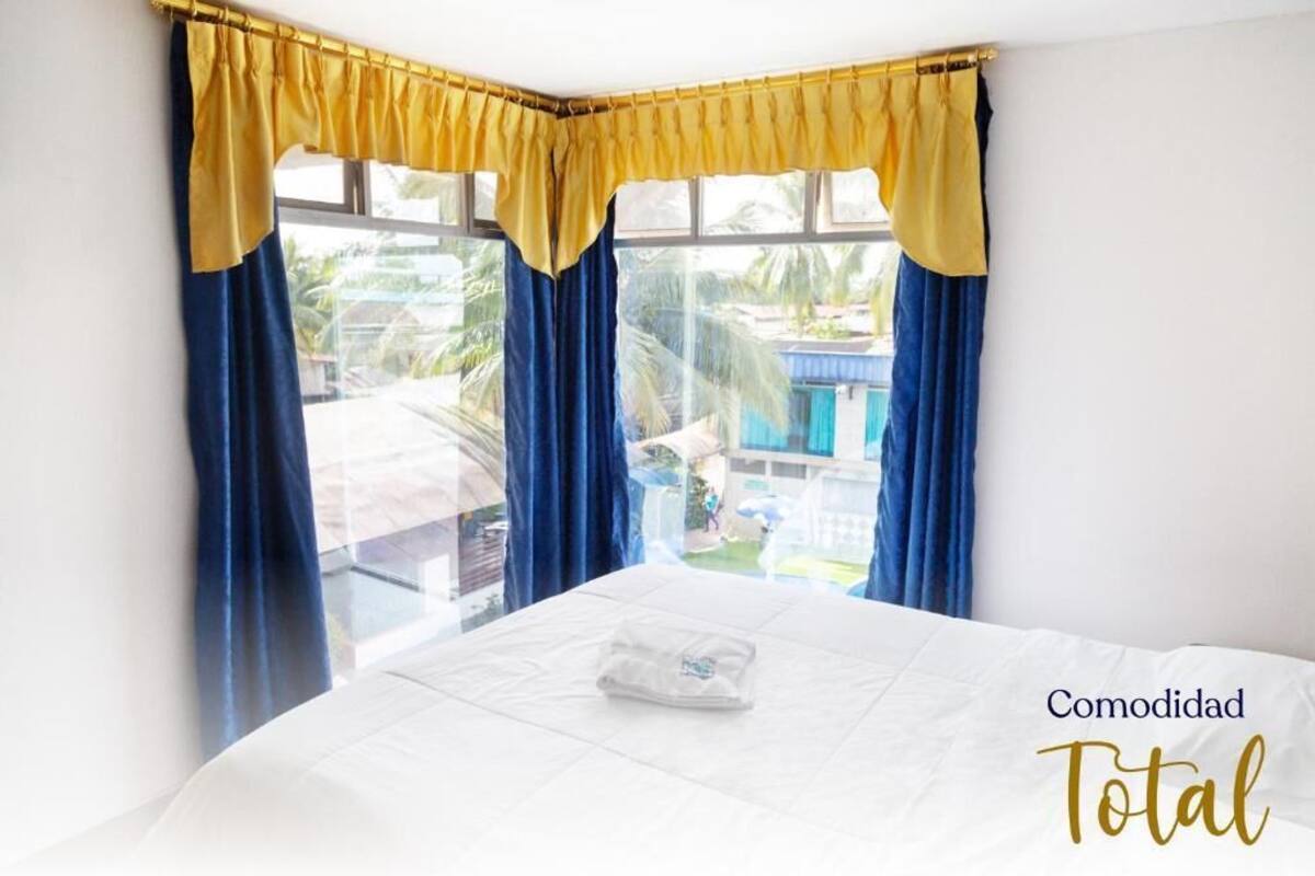 A bedroom with a bed, a window with yellow and blue curtains, and a view of a house outside.