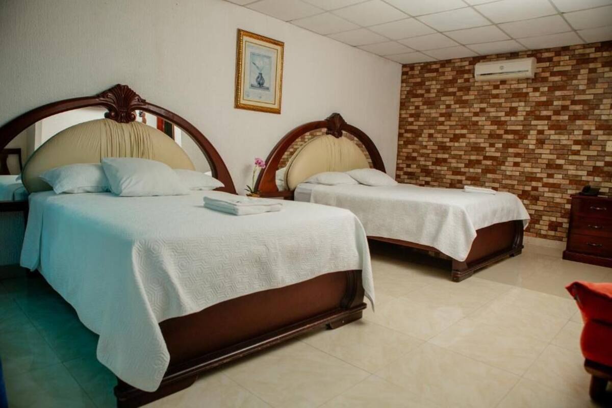 A hotel room with two beds, a brick-patterned wall, and an air conditioning unit.