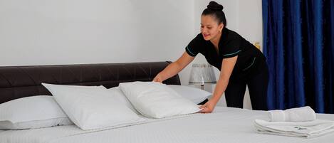 A neatly made bed with white linens and pillows, a folded towel, and a bedside lamp.