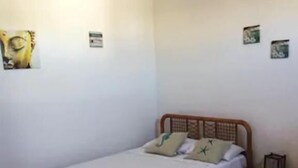 Uma cama de solteiro com cabeceira de madeira, mesa de cabeceira pequena e prateleira fixa na parede.