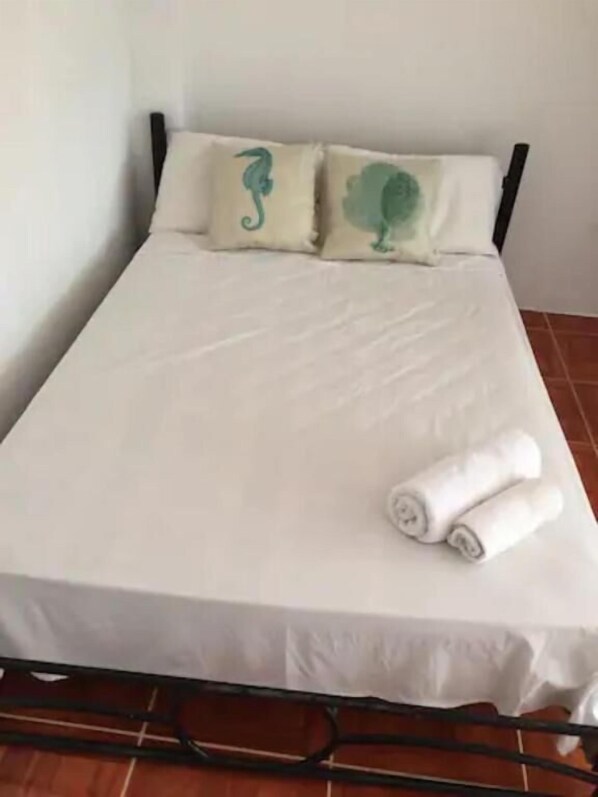 A bed with a white mattress and two pillows with green designs, a rolled white towel on the bed, and a metal frame.