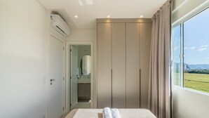 Ein Hotelzimmer mit Bett, Kleiderschrank, Klimaanlage und Fenster mit Blick auf eine grüne Landschaft.