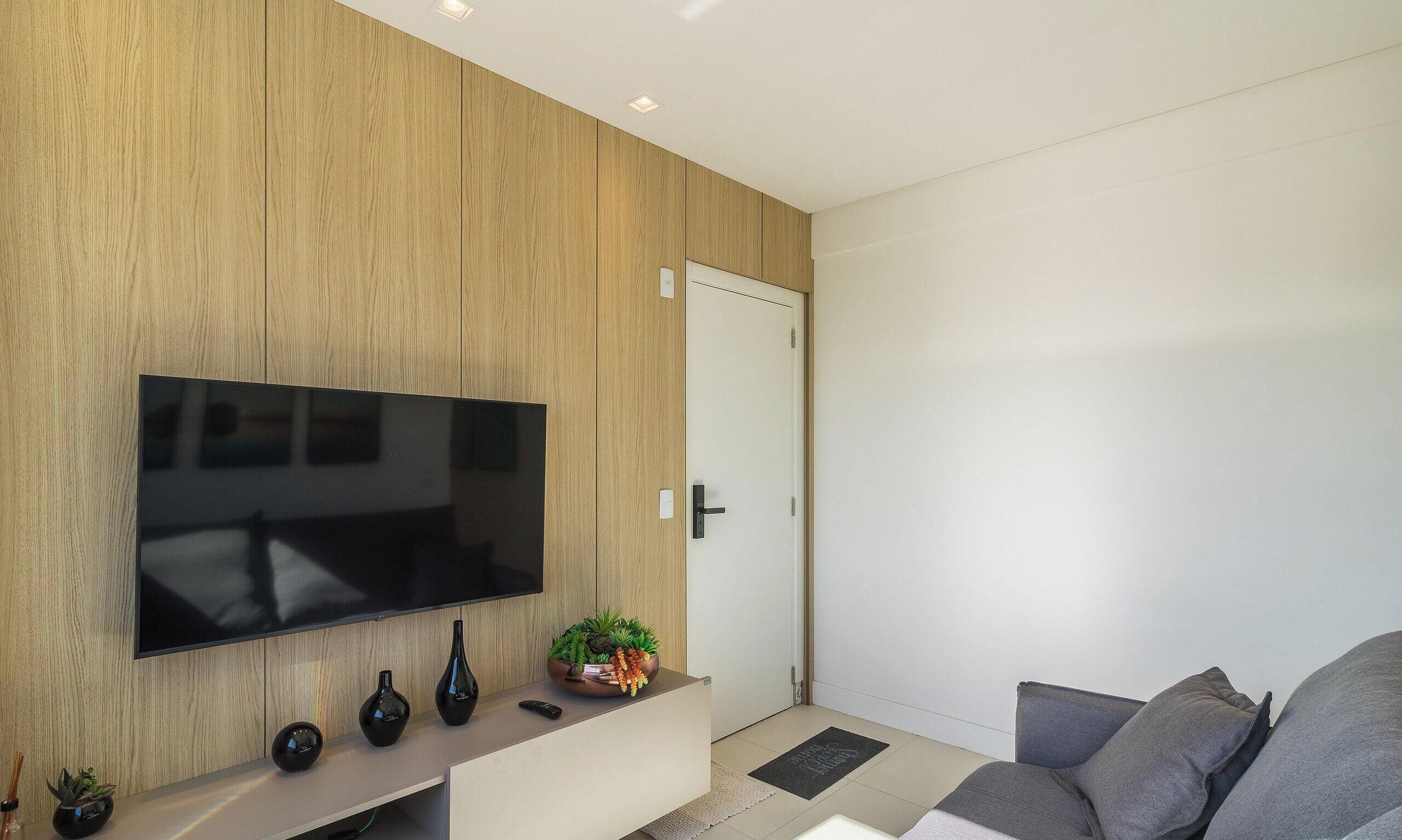 Ein modernes Wohnzimmer mit einem an einer Holzwand montierten Flachbildfernseher, einem grauen Sofa und einem kleinen Konsolentisch mit Dekoration.